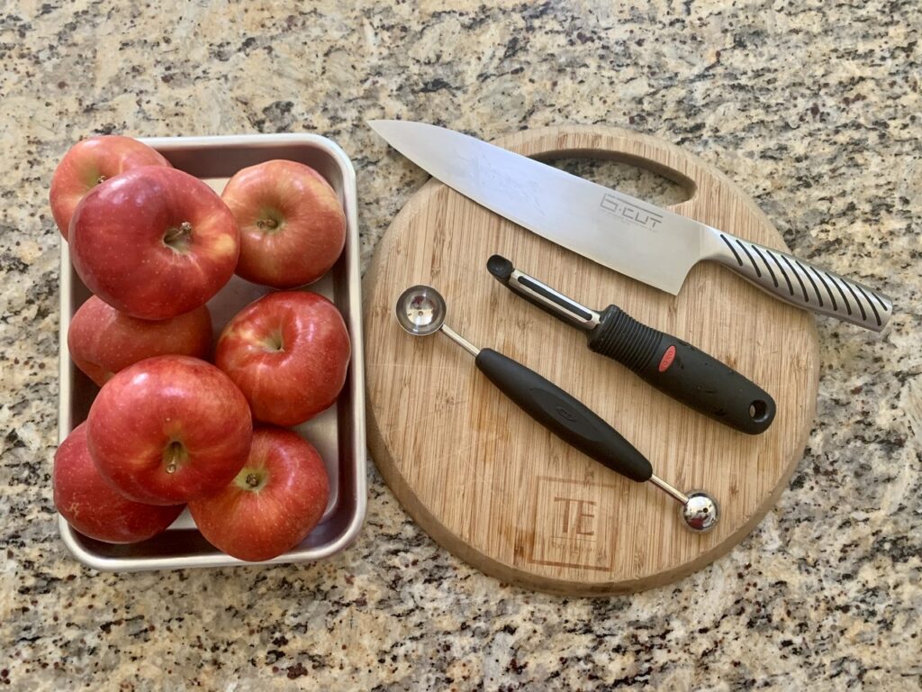 Apples, peeler, melon baller, knife and cutting board 