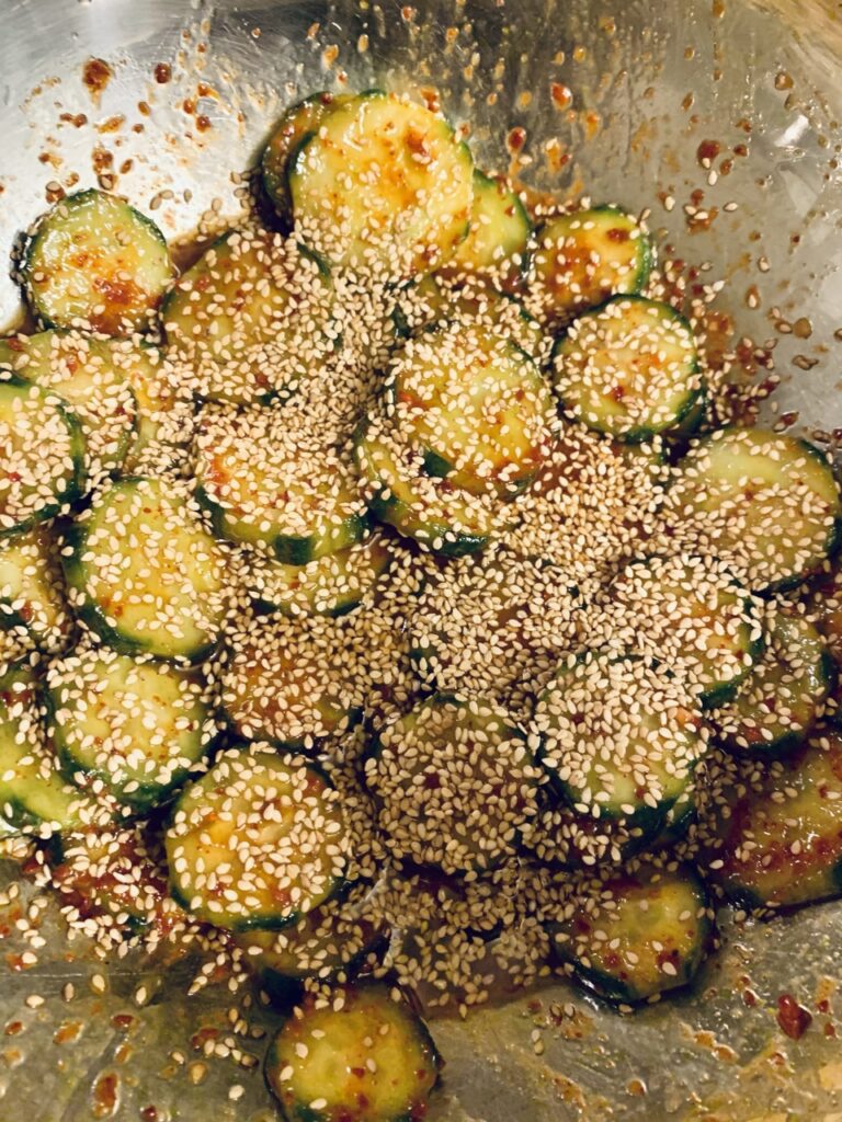 Finally adding toasted sesame seeds to marinated cucumber coated with dressing to make Oi Muchim